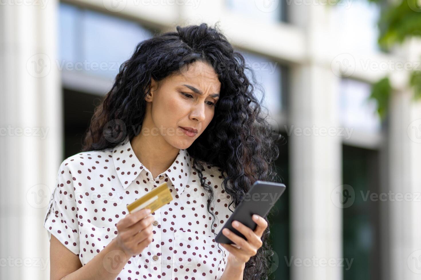Upset and disappointed woman received money transfer error, Hispanic woman with bank credit card and phone cheated walking down street outside office building. photo