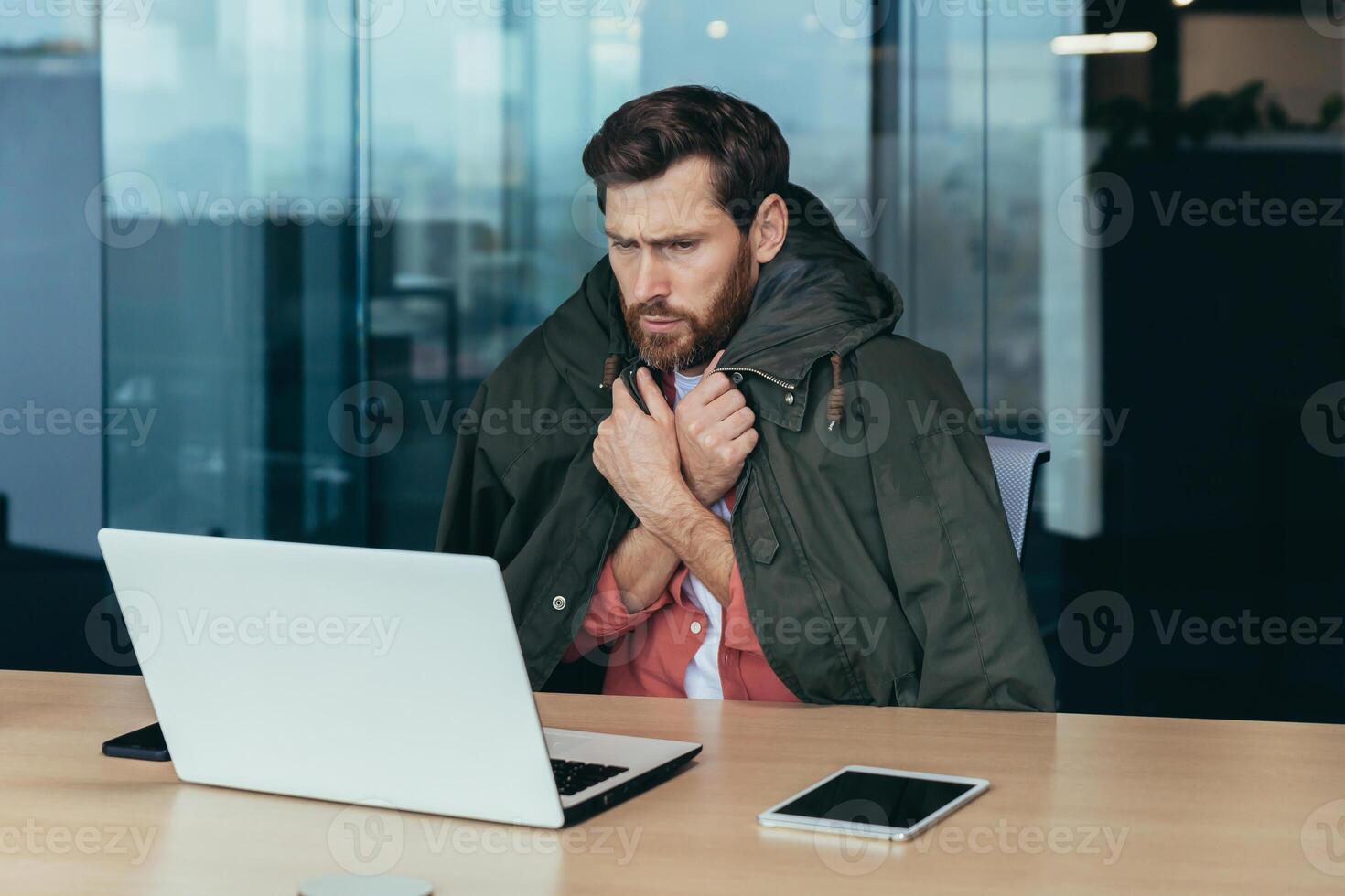 It's cold in the office, the businessman is freezing while working on a laptop inside the building, the man is covered with a warm jacket. photo