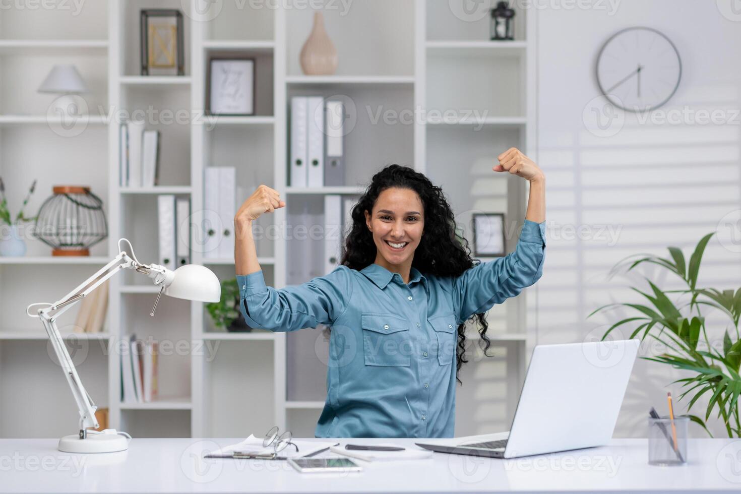 A joyful Hispanic woman working from home celebrates a business achievement in her modern office setup. photo