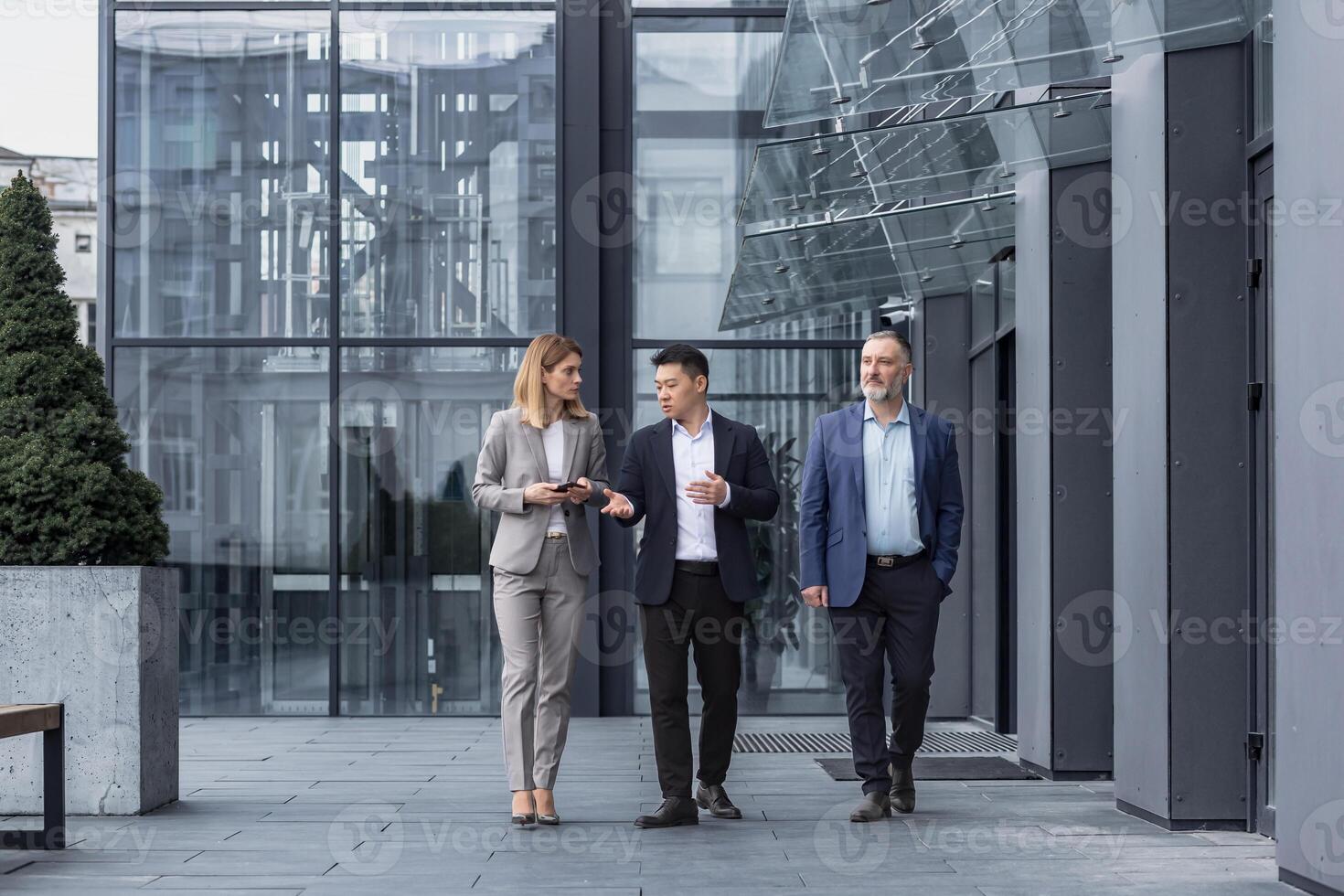 Three diverse business people walking and talking focused and thoughtful seriously outside office building, male and female, discussing plans and work project photo