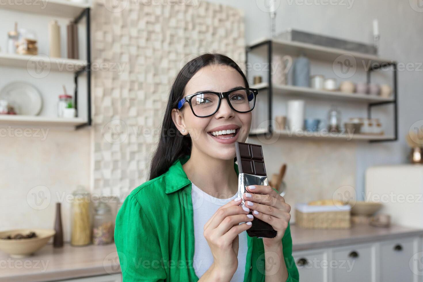 Portrait of a woman holding and eat a bar of black chocolate. Standing at home in the kitchen photo