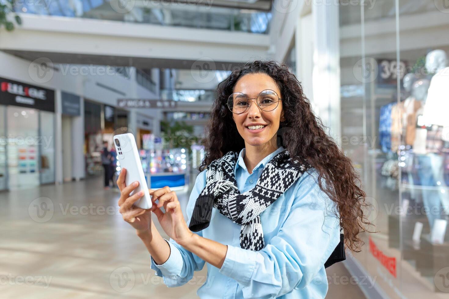 Shopping on a trip. Young Hispanic woman is traveling, shopping in a supermarket, holding a phone photo