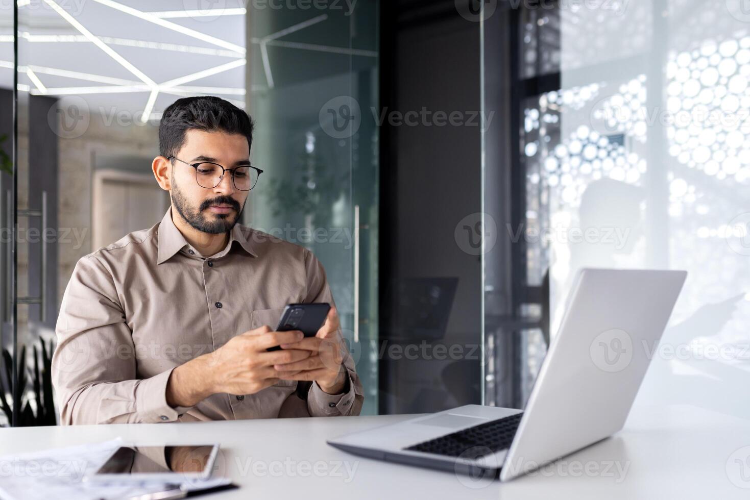 Serious concentrated businessman at the workplace inside the office, the man holds a smartphone in his hands, a worker with a laptop browses the Internet and social networks, types a text message. photo