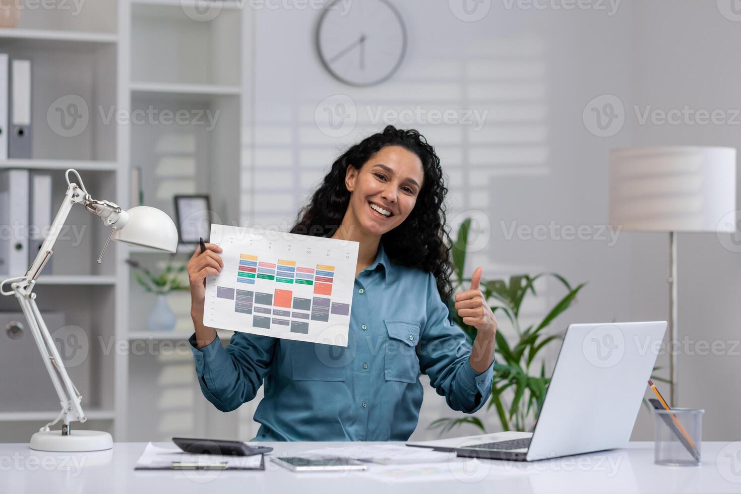 Cheerful Hispanic businesswoman presenting a colorful report and giving a thumbs up from her tidy home office setup. photo
