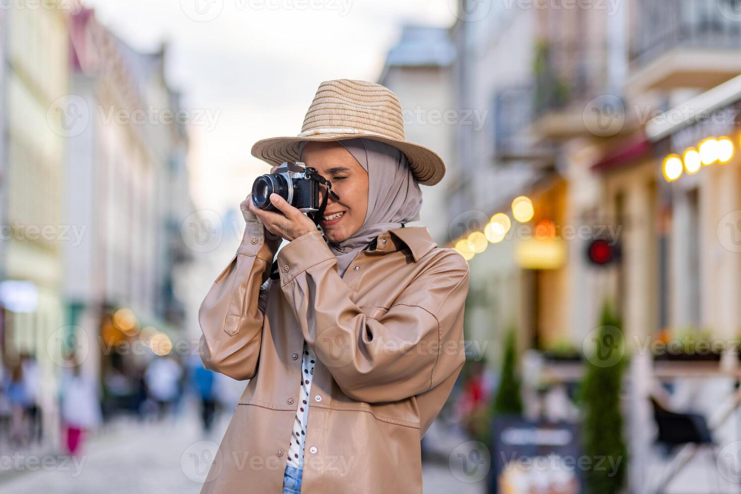 Young beautiful woman walking in the evening city in hijab, tourist with camera and wearing a hat inspects the historical city smiling with satisfaction, Muslim woman on a trip. photo