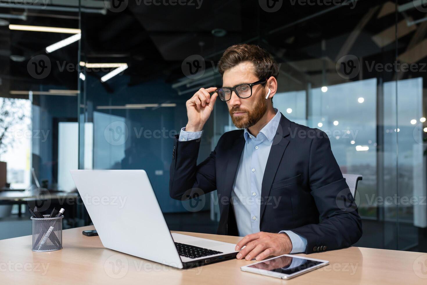 Mature serious thinking businessman working inside office, boss investor in business suit working at table with laptop brainstorming business strategy and plan. photo