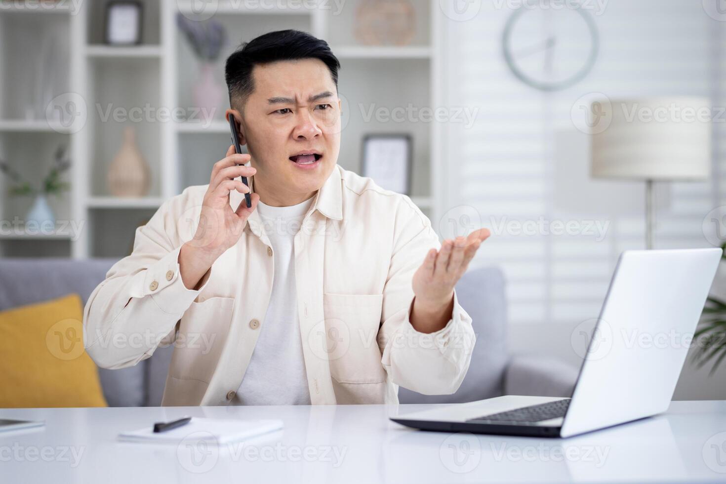 enojado enojado y trastornado hombre hablando en teléfono a hogar, asiático trabajando remotamente desde hogar oficina sentado a mesa en vivo habitación, Lanza libre empresario a trabajar. foto