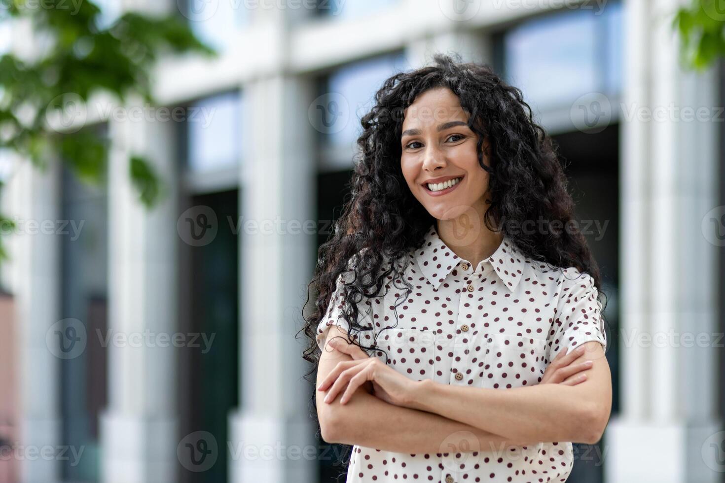 un profesional mujer de negocios soportes con confianza con su brazos cruzado en contra un corporativo edificio fondo, exudando fortaleza, liderazgo, y éxito. foto