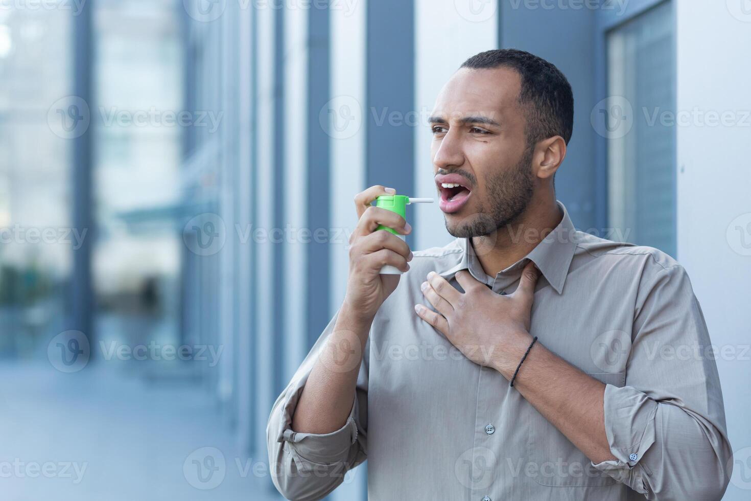 A young Latin American man clears his throat with an inhaler and medication. He stands outside photo