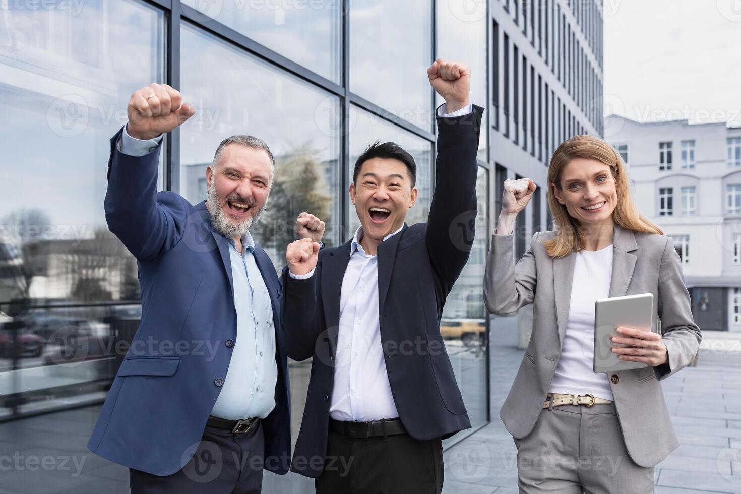 Successful diverse business team, three loving men and woman looking at camera and happy celebrating victory, team dreaming outside office building, business group in business suits photo