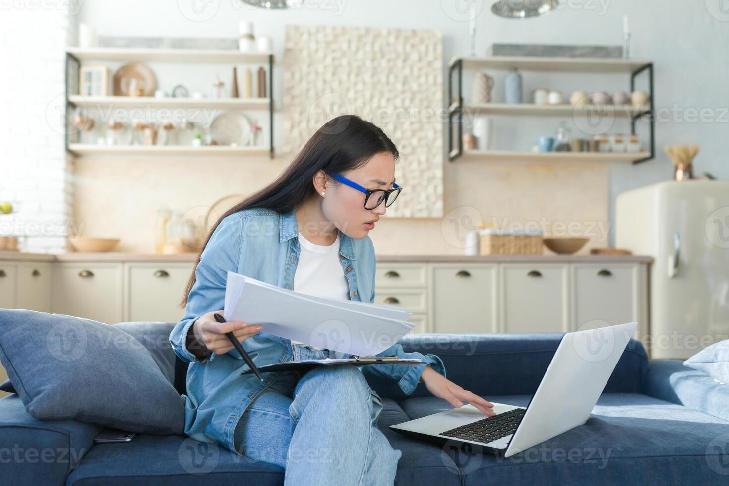 Frustrated and sad business woman at home doing paper work, Asian woman disappointed with work result, using laptop to calculate bills and household budget photo