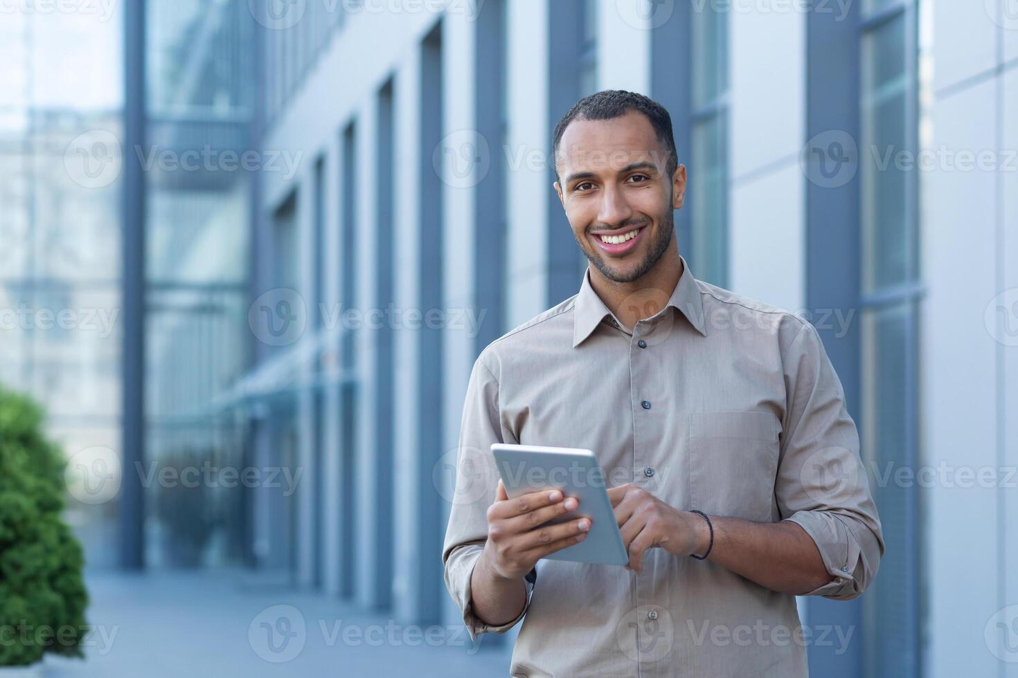 Portrait of a happy businessman outside an office building, a man in a casual shirt is looking at the camera and smiling, a businessman is using a tablet computer photo