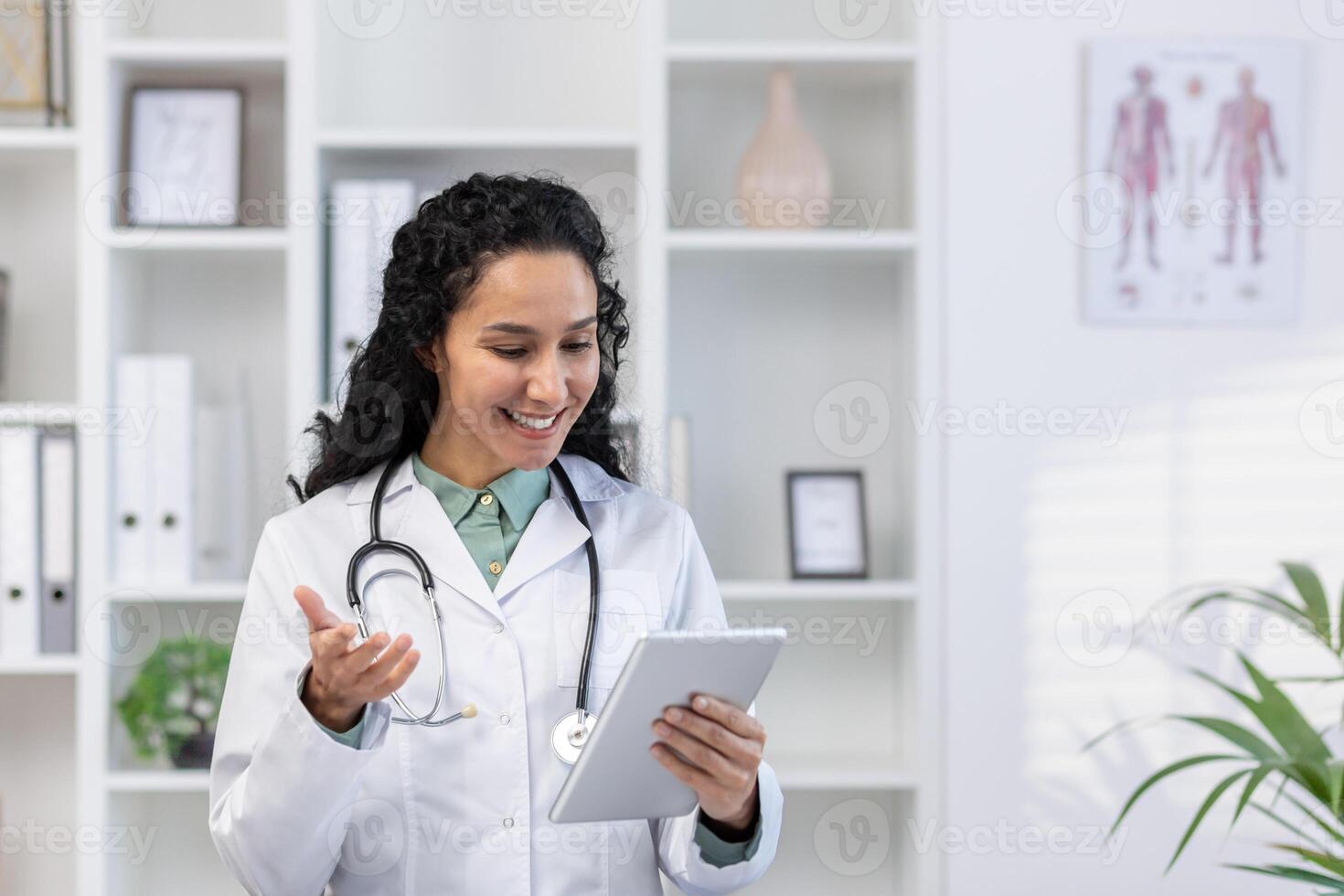 Doctor inside the medical office stands with a tablet computer in hands, a clinic worker in white medical robe will advises the patient remotely using the for call, joyfully and friendly. photo