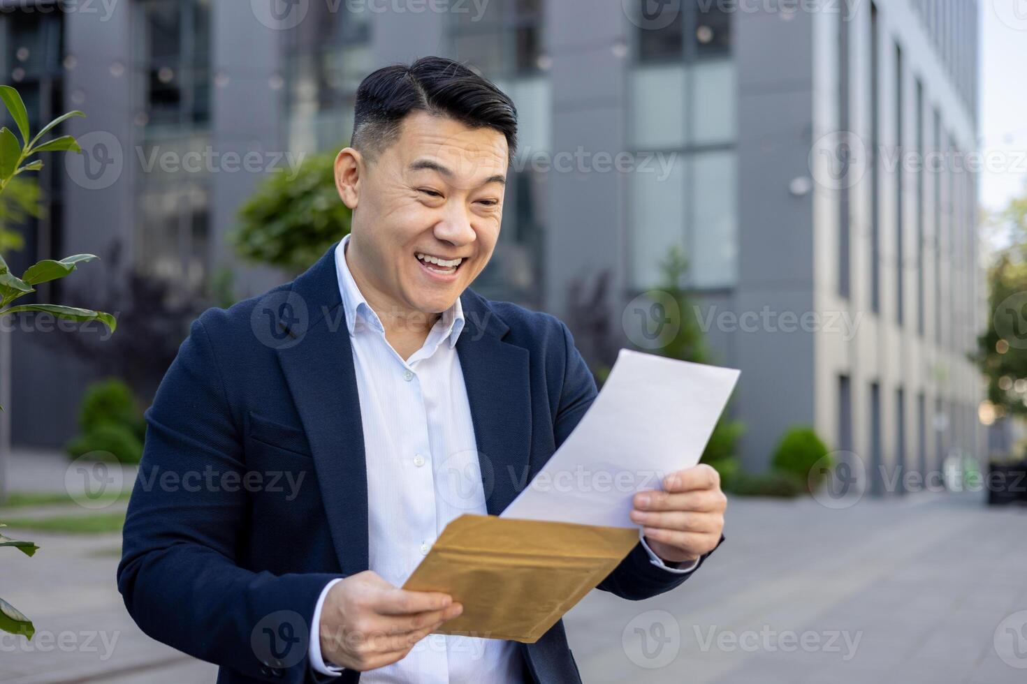 contento asiático empresario leyendo un letra con emoción fuera de un oficina edificio, expresando éxito y alegría. foto