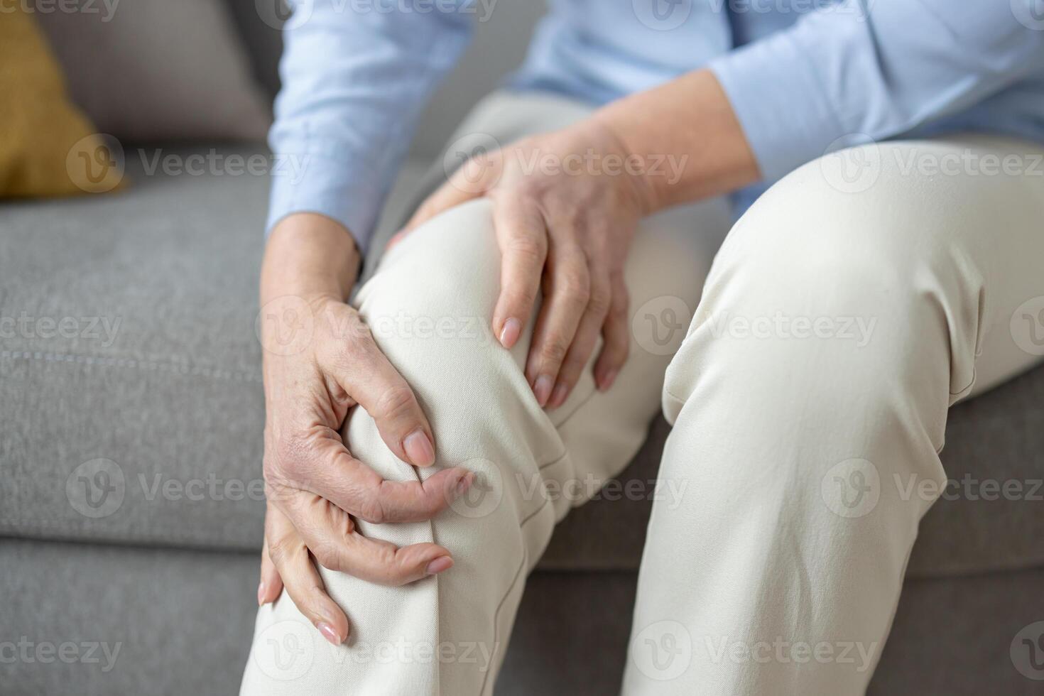 Senior woman sits in a living room, gently holding her sore knee, depicting common age-related health issues and the need for elderly care. photo
