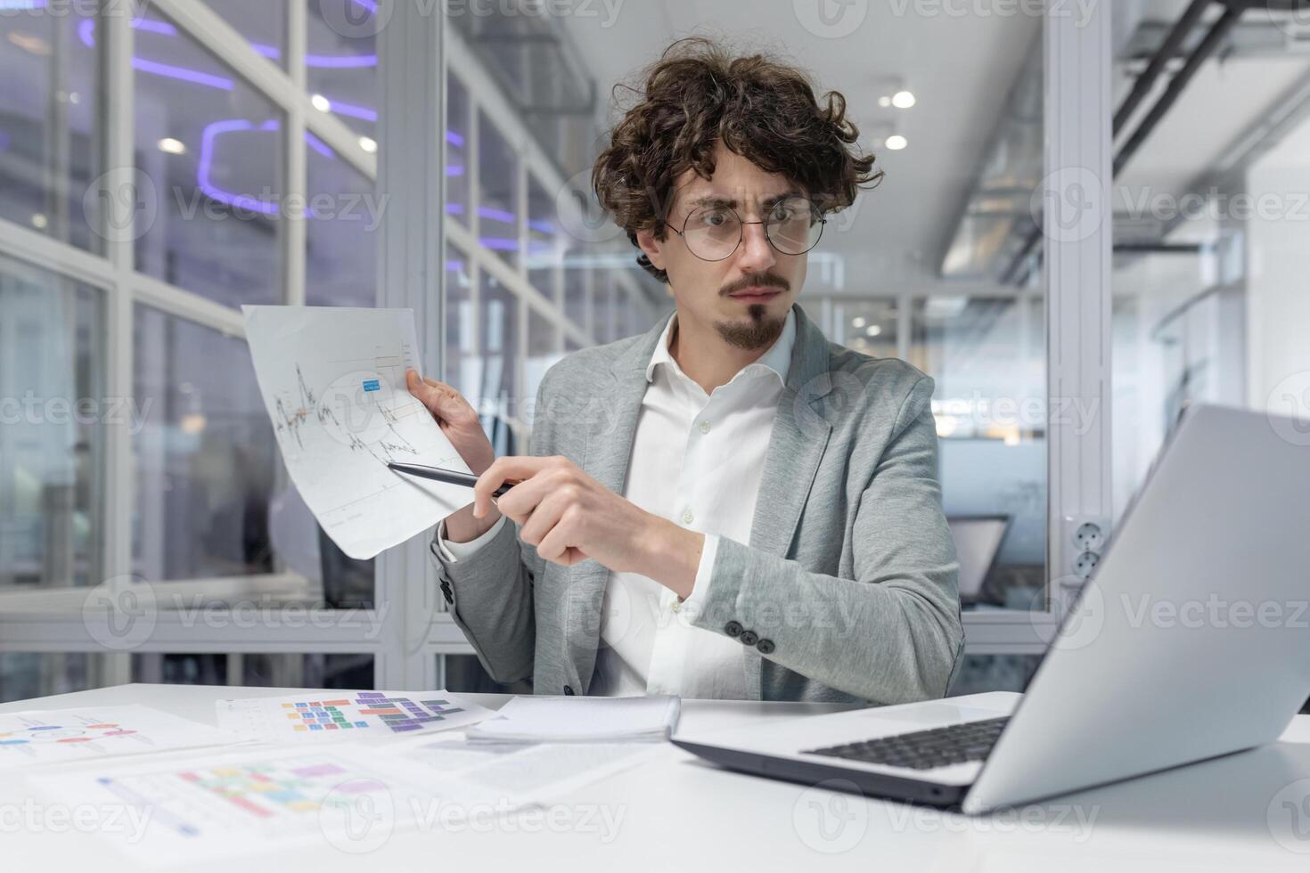 Focused young adult office worker examines important business documents, showcasing analytical skills in a professional office environment, conveying concentration and dedication. photo