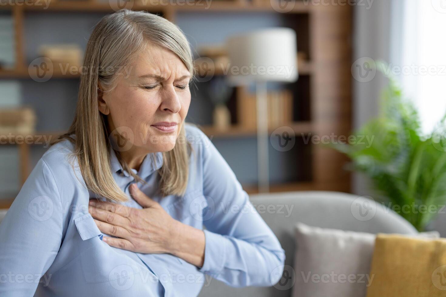 Mature woman experiencing discomfort and holding her chest due to pain. She seems anxious and worried, possibly indicating a health issue. photo