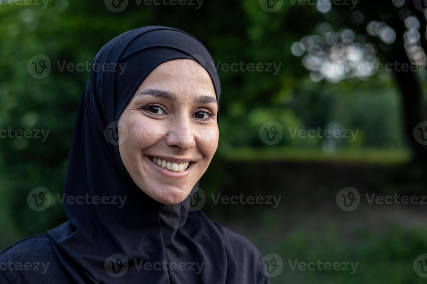 retrato de un contento musulmán mujer vistiendo un hijab al aire libre con un natural verde fondo, exhibiendo cultural diversidad y alegría. foto