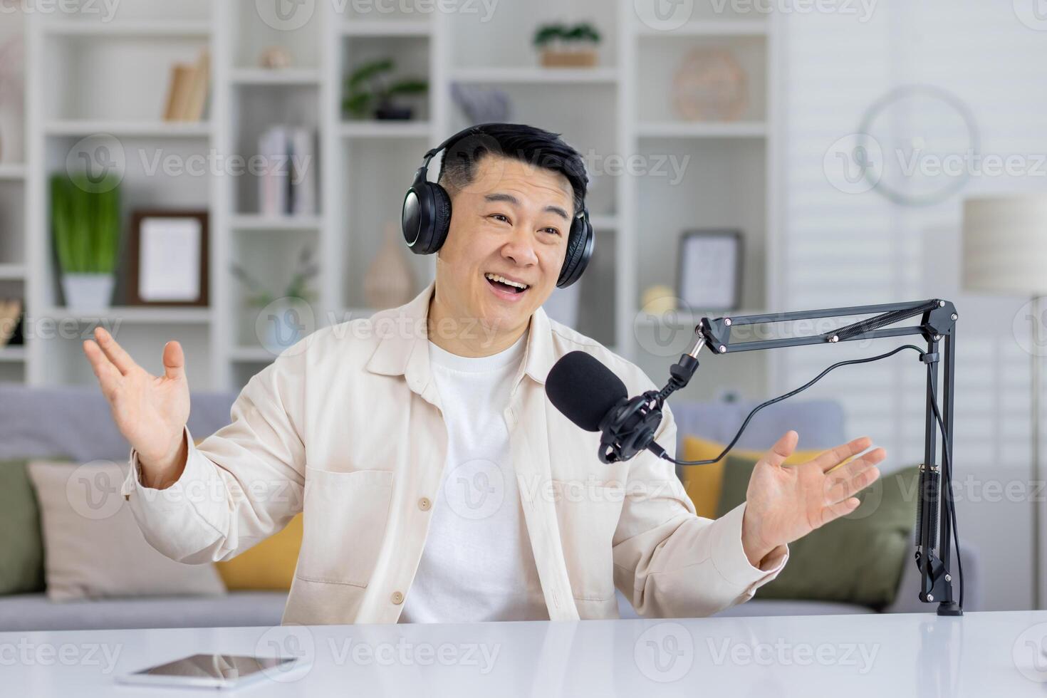 Enthusiastic Asian podcaster talking with hands, having an engaging conversation indoors, looking at camera with headphones and microphone. photo