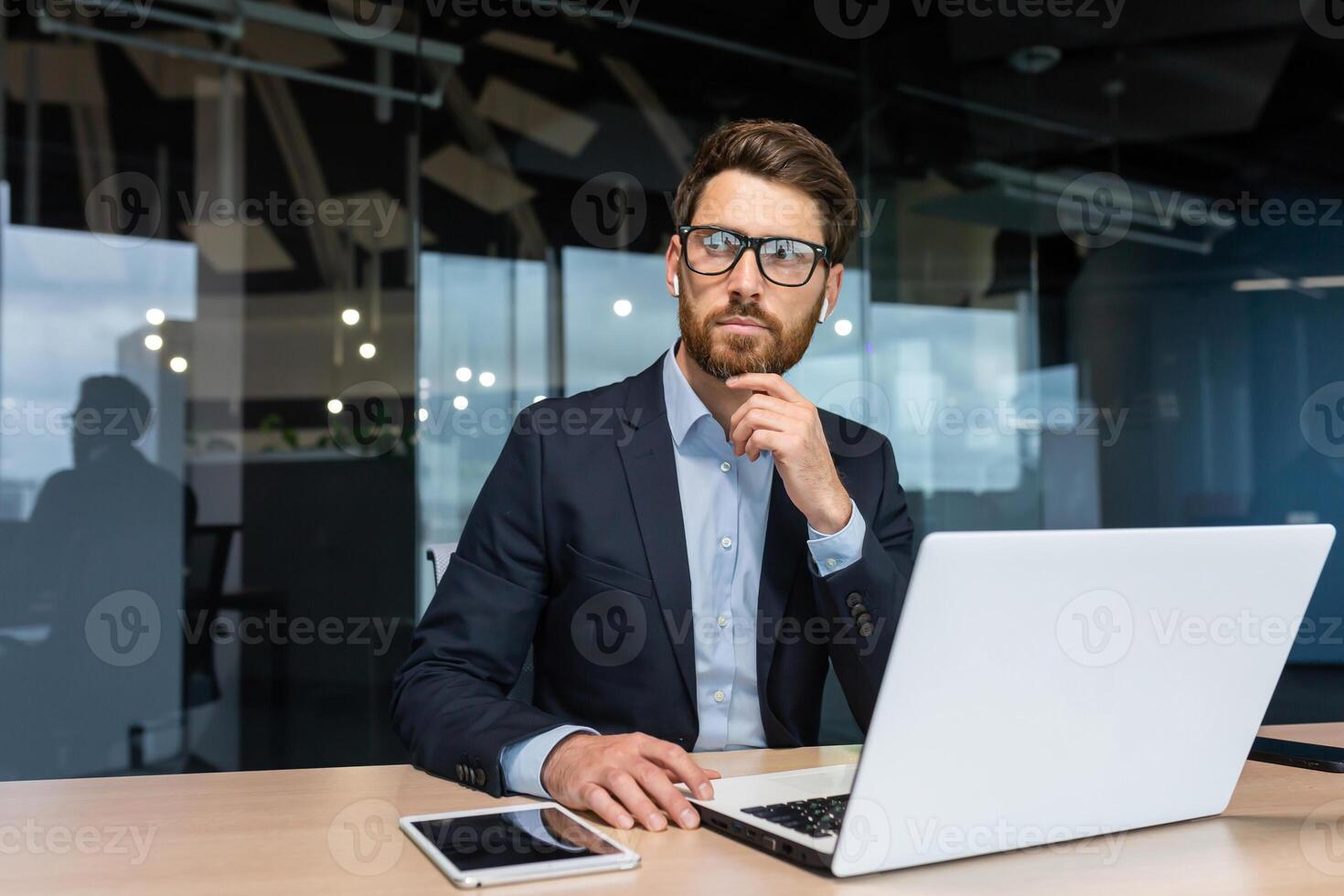Mature serious thinking businessman working inside office, boss investor in business suit working at table with laptop brainstorming business strategy and plan. photo