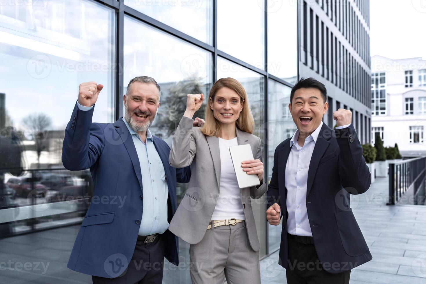 Successful diverse business team, three loving men and woman looking at camera and happy celebrating victory, team dreaming outside office building, business group in business suits photo
