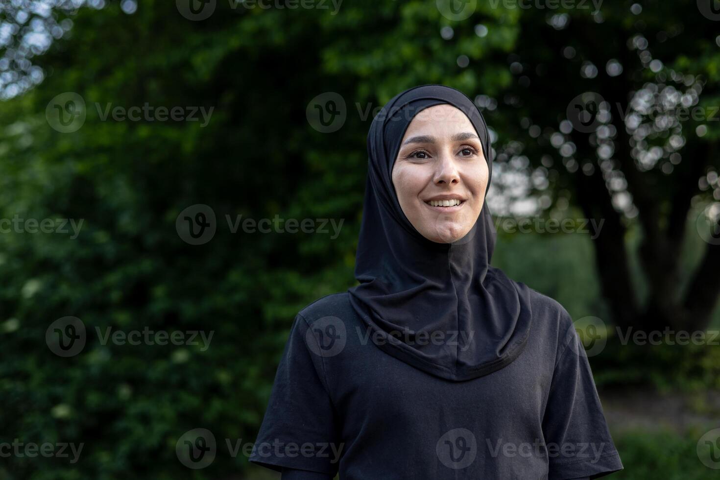 Portrait of a smiling muslim woman wearing a hijab outdoors, exuding confidence and serenity in a tranquil park setting with green foliage background. photo