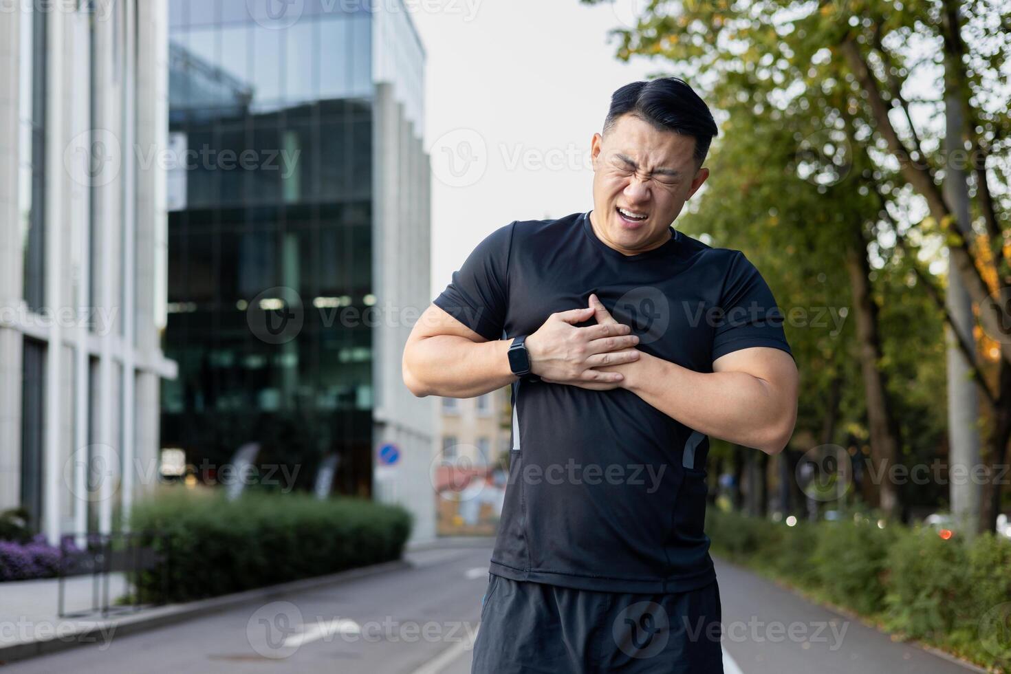 joven asiático hombre haciendo Deportes a el estadio. él es en pie doblado encima, participación su mano a su pecho, sufrimiento desde dolor, corazón ataque, cansancio excesivo. foto