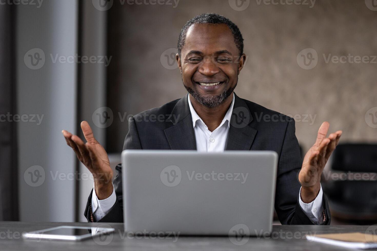 satisfecho empresario mirando felizmente a portátil computadora pantalla y extensión manos mientras sonriente ampliamente. oscuro peludo hombre sensación satisfecho mientras viendo resultado de diario difícil trabajo a hogar oficina. foto