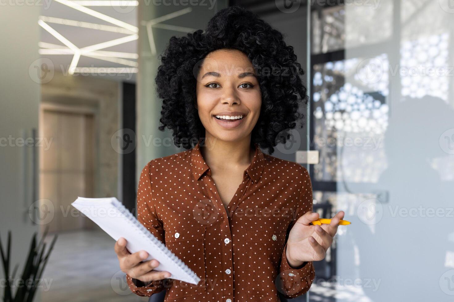 africano americano mujer de negocios atractivo en un llamar. ella es participación documentos y sonriente a el cámara en un bien iluminado, contemporáneo oficina espacio. foto