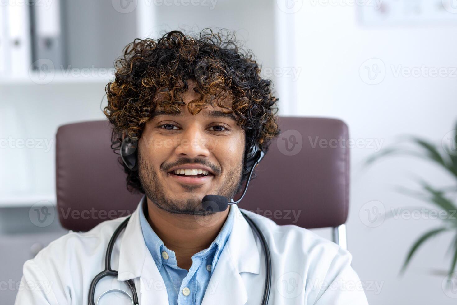 Webcam view, young doctor with headset phone using laptop for call, doctor cheerfully and friendly consulting patients, smiling and looking at camera, working inside clinic medical room. photo