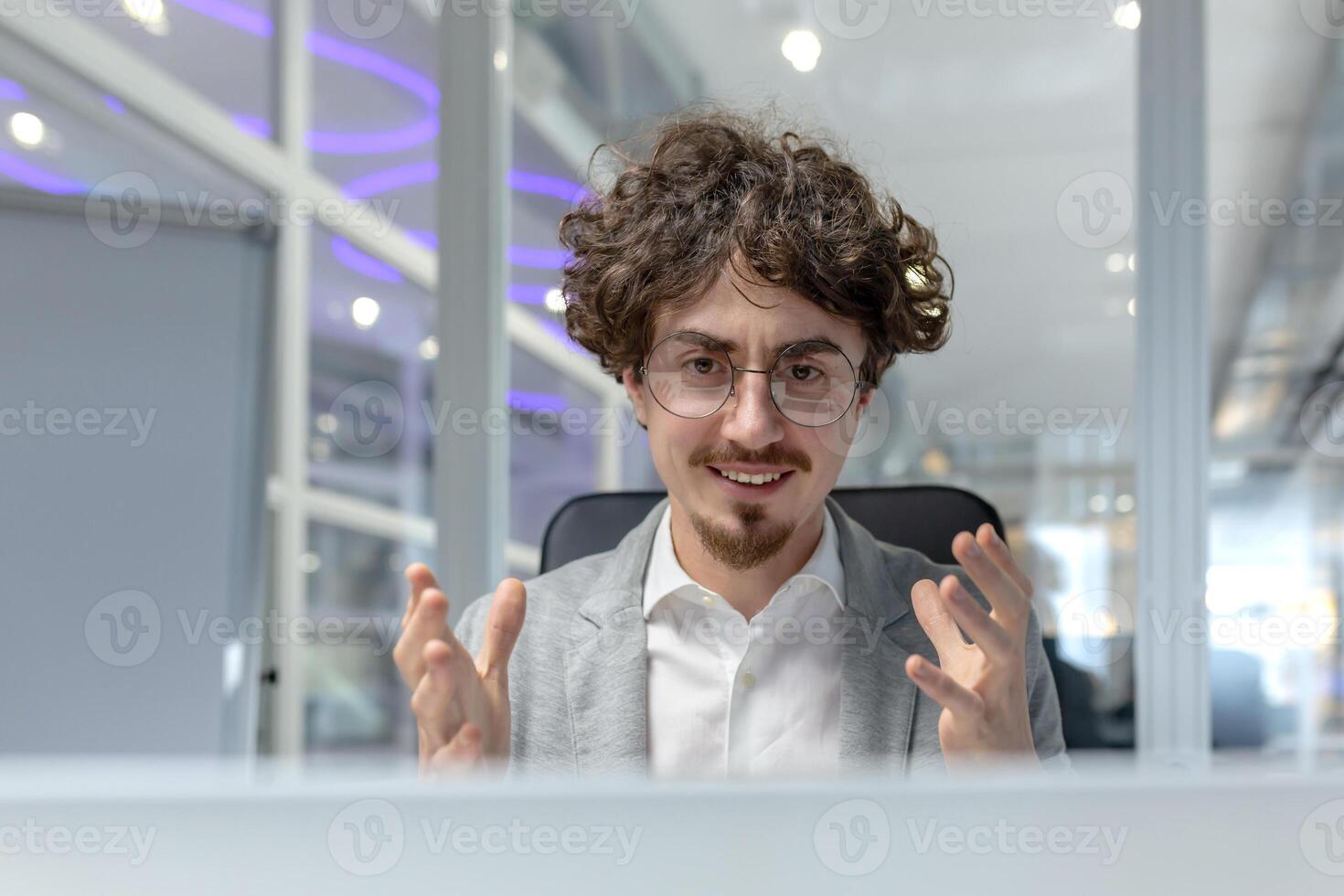 A curly-haired young businessman focuses on a discussion while working in a modern office environment, embodying corporate determination. photo