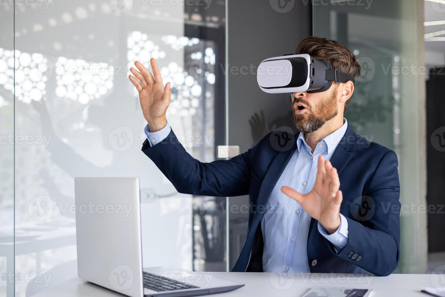 Businessman in suit using VR headset at office desk, experiencing virtual reality technology with expressive hand gestures. photo