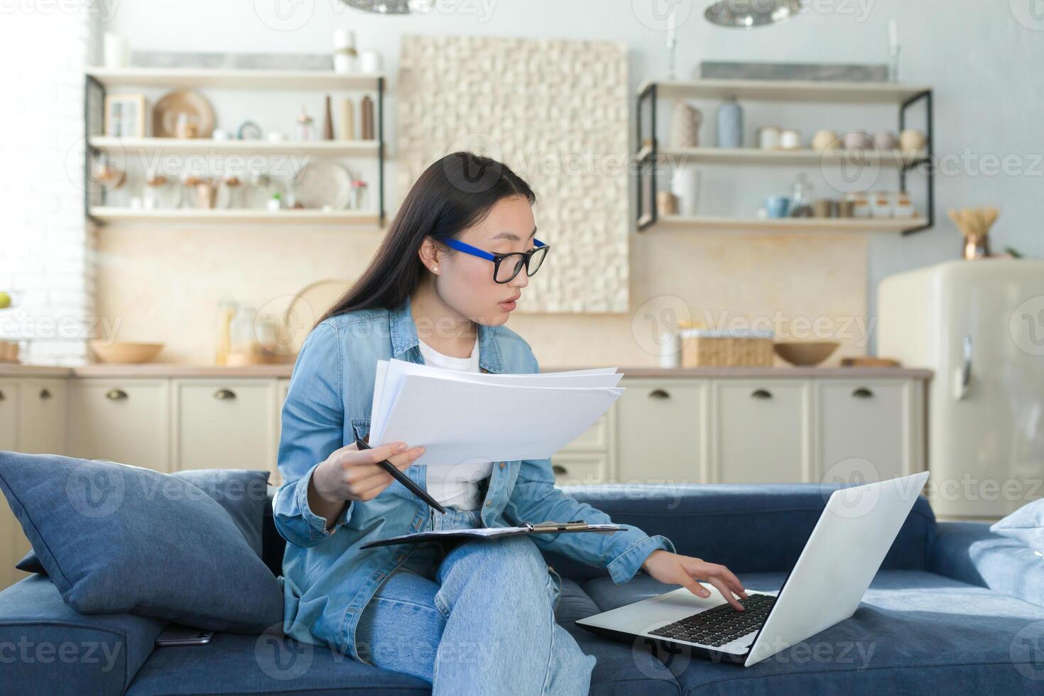 trabajo a hogar en línea. joven asiático hembra contador trabajando a hogar. sentado en el sofá con un ordenador portátil y documentos. foto