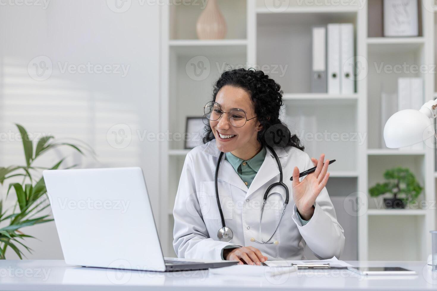 A cheerful hispanic female doctor is seen talking to a patient during a call consultation from her office. photo