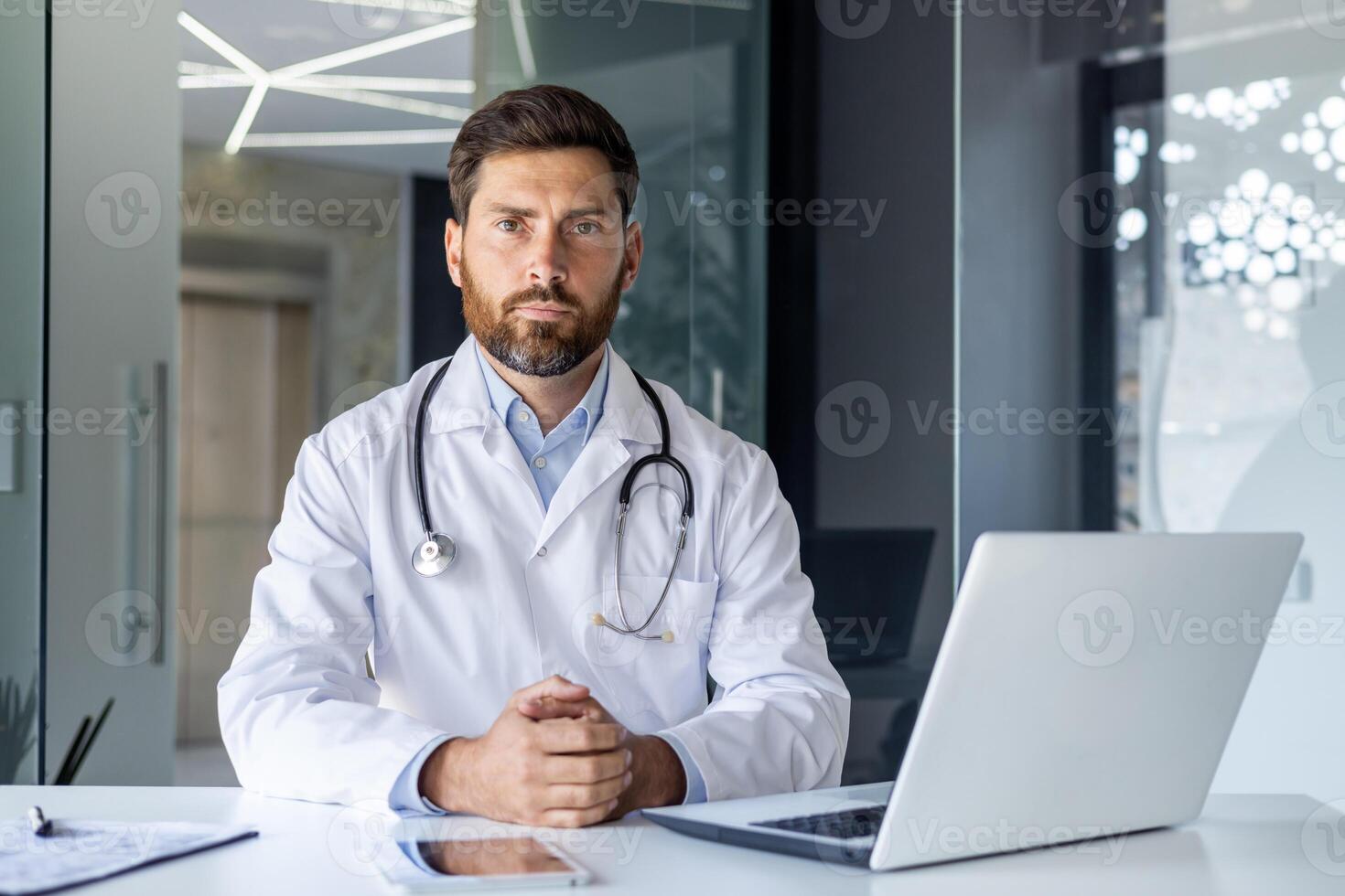 Portrait of a young male doctor sitting in a slaughterhouse office at a desk in a white coat, looking seriously and focused into the camera. photo