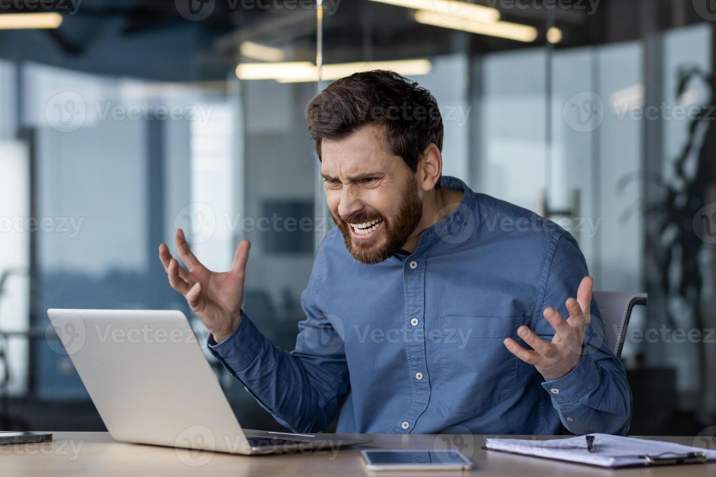An angry businessman is feeling frustrated with technology, showing stress and aggression towards his laptop in an office environment. photo