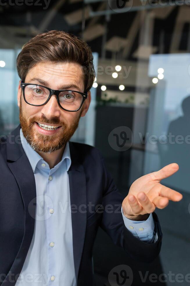 Vertical shot, a businessman in the office is talking to colleagues and friends using an application on a smartphone, a mature man in a business suit inside the office is smiling friendly. photo