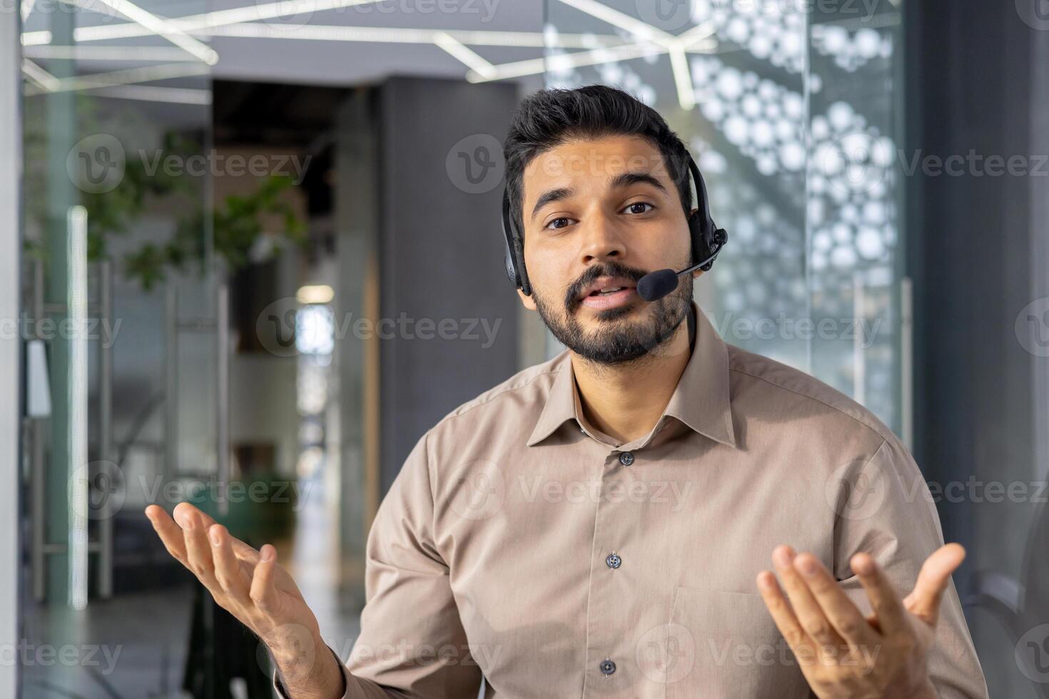 An engaging Indian businessman communicates while wearing a headset, showcasing his professional demeanor and expert communication skills in a stylish office setting. photo