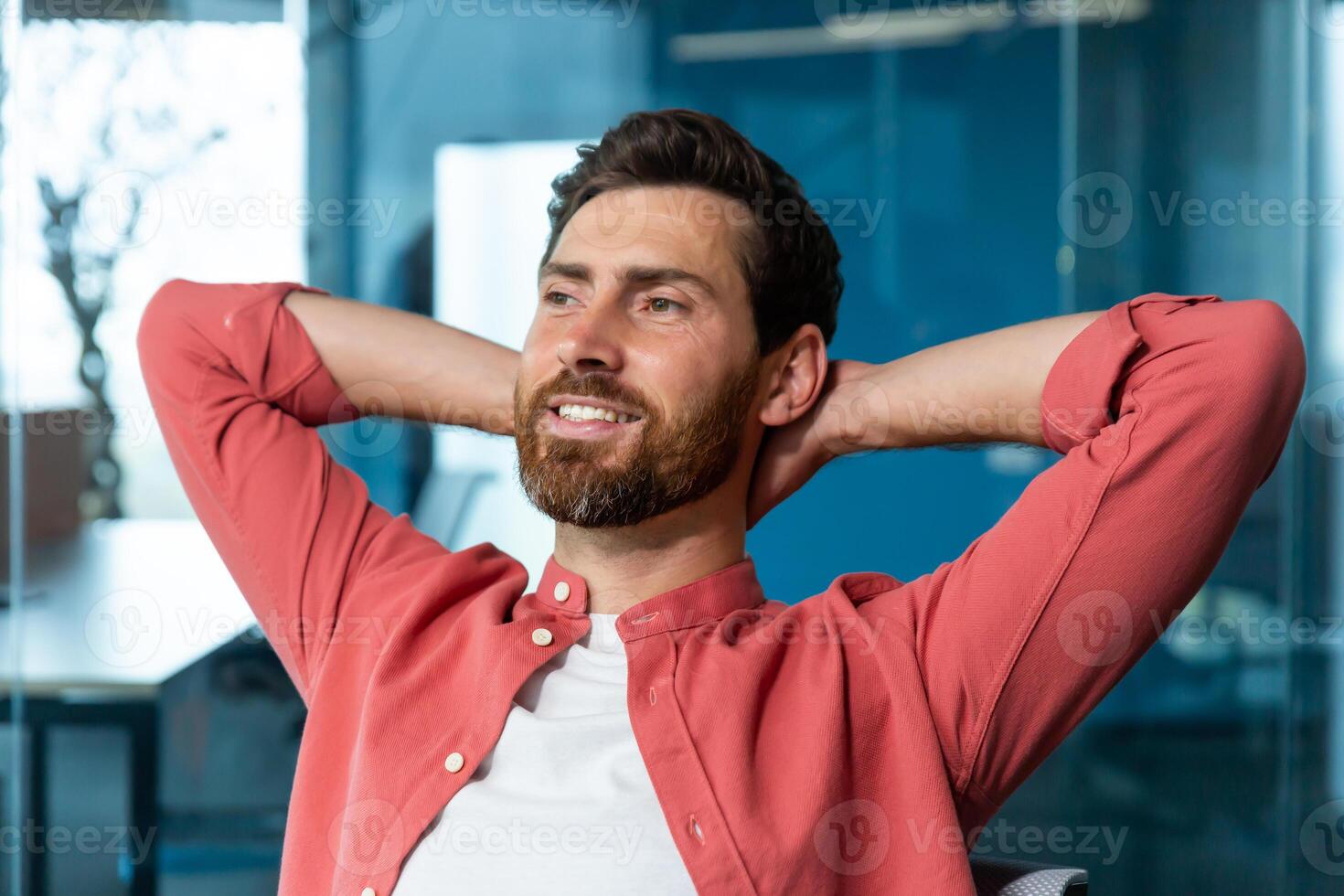 Young successful businessman startuper rests in office, man in red shirt throws hands behind head and dreams visualizes, designer thinks about new project. photo