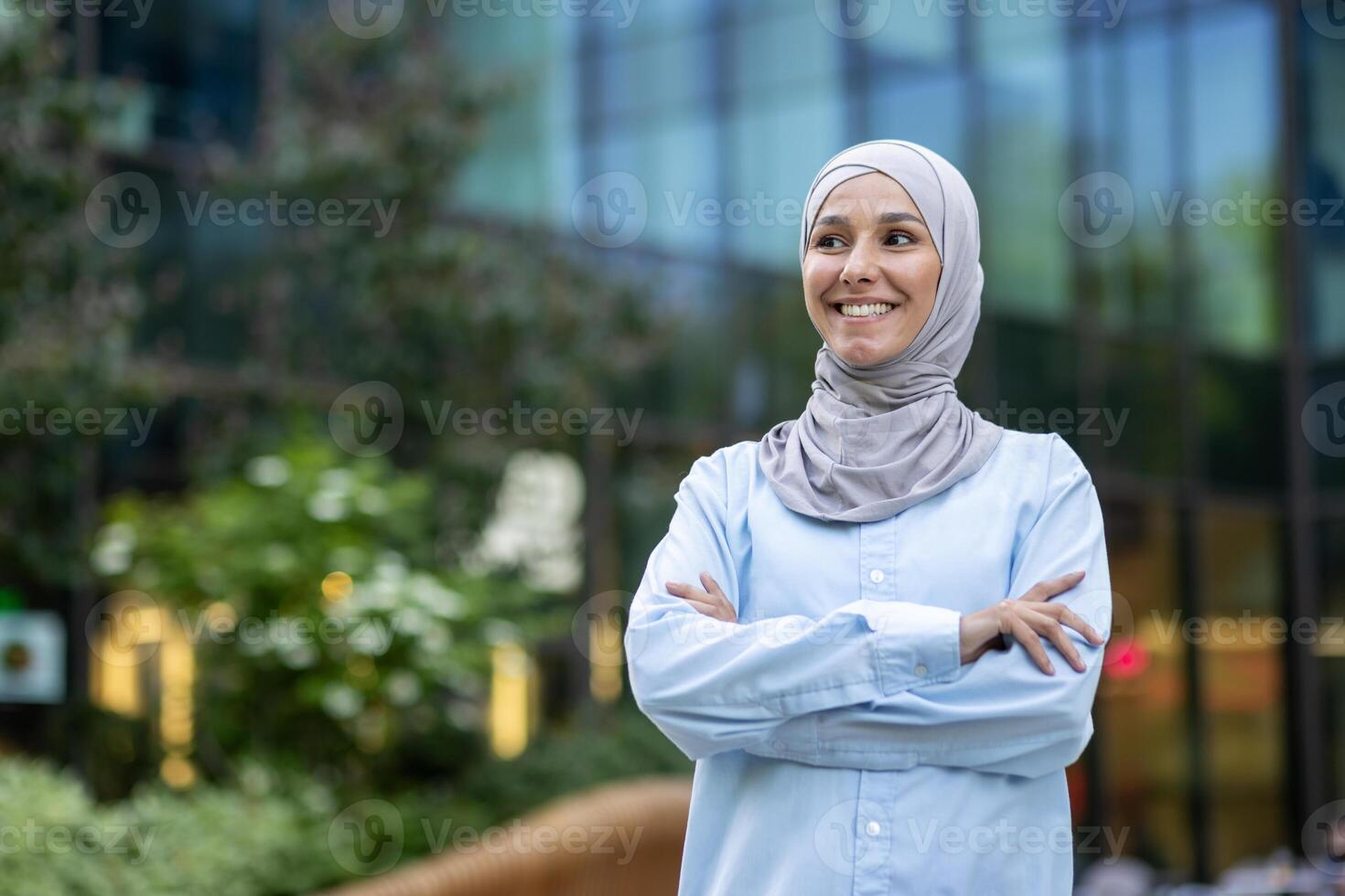 un profesional joven mujer vistiendo un hijab con confianza sonrisas en contra un moderno oficina edificio fondo, encarnando inclusividad y diversidad en el lugar de trabajo. foto