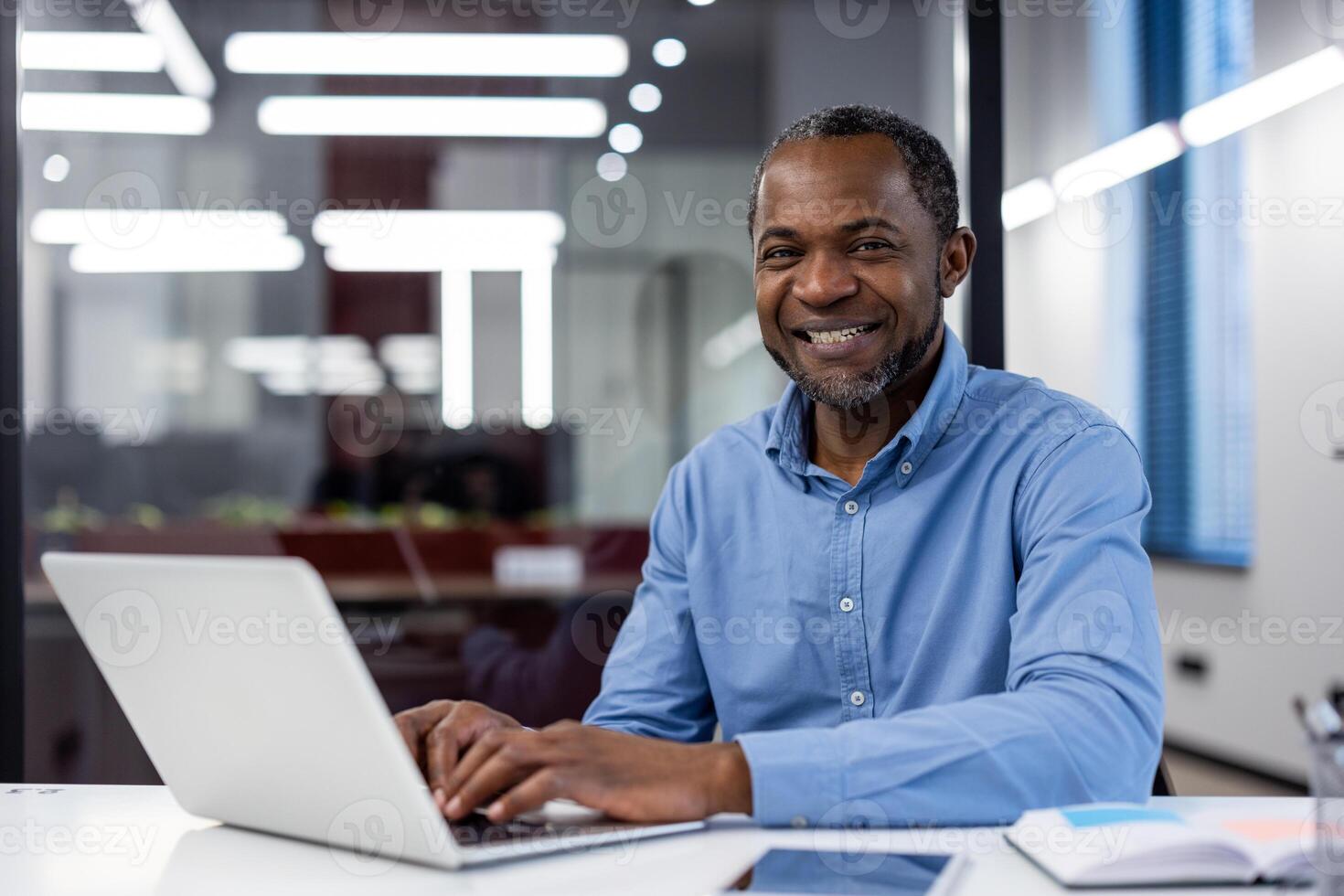 profesional africano americano masculino empresario con un radiante sonrisa a su oficina escritorio utilizando un ordenador portátil. foto