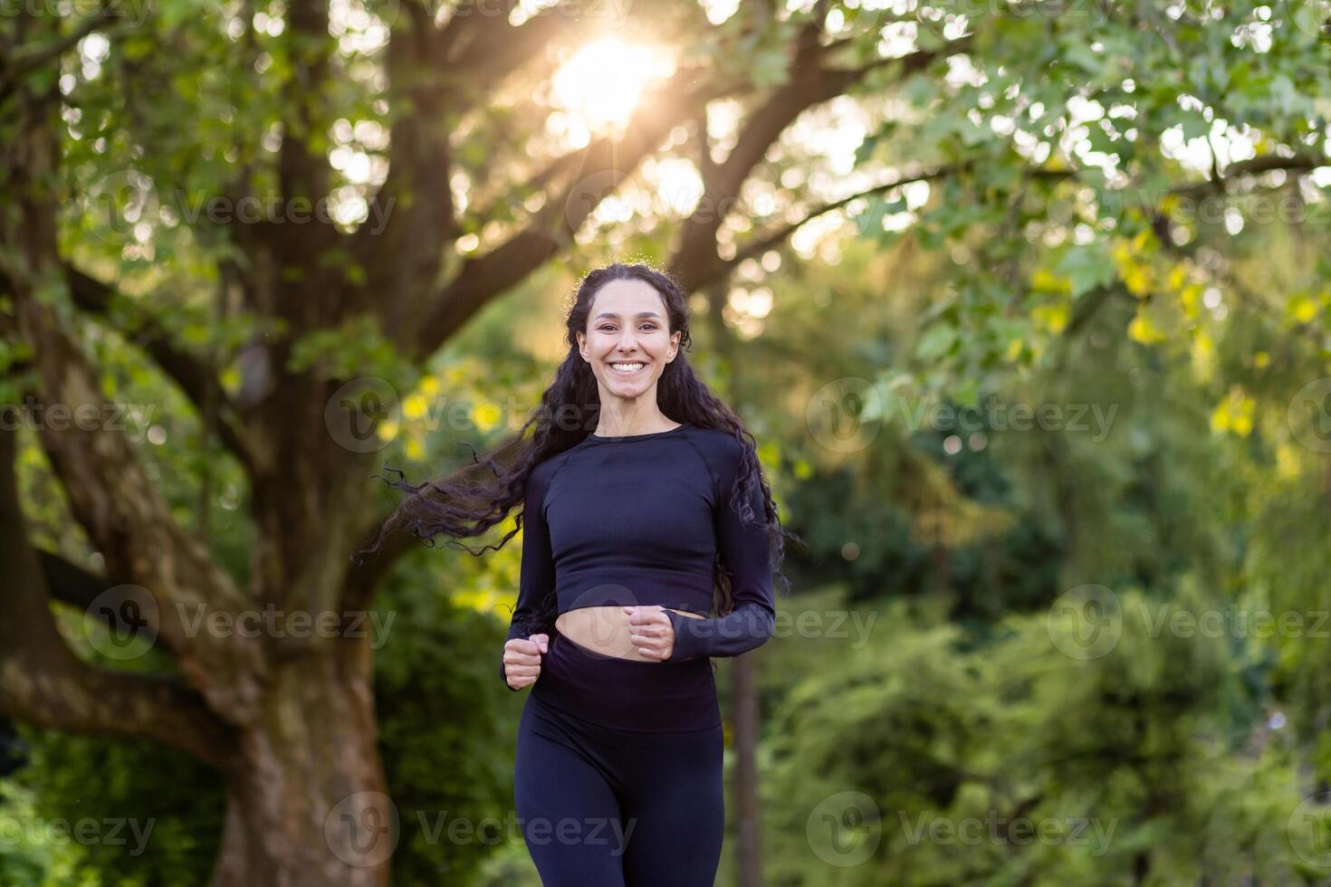 Young beautiful woman running in the park, portrait of a Latin American woman jogging and doing active exercises, sportswoman smiling and looking at the camera among the trees. photo