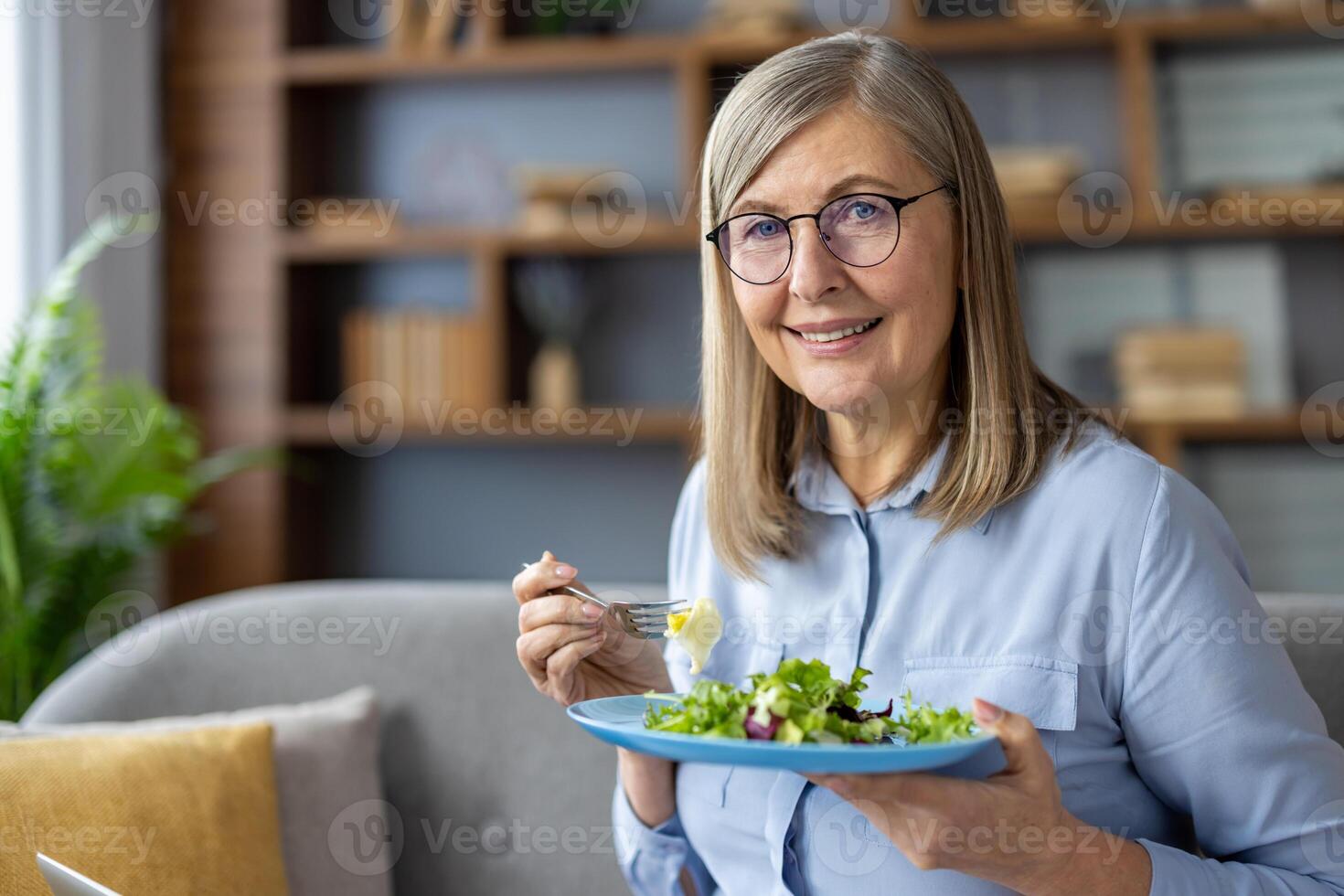 Portrait of mature woman at home, woman smiling and looking at camera with plate of healthy food, salad, healthy eating diet. photo