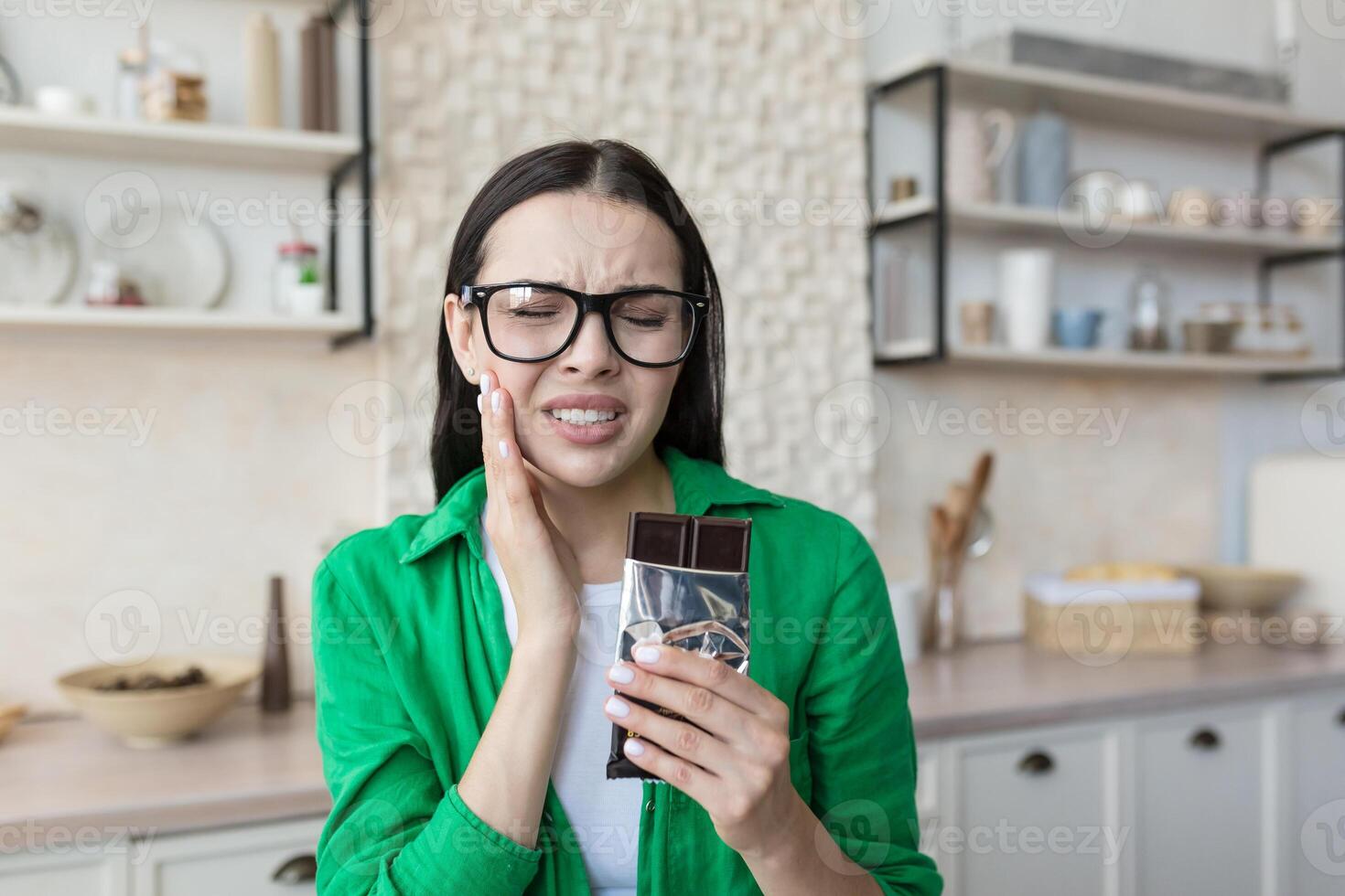 A young woman eating a bar of dark chocolate at home. Holds his cheek, feels a strong toothache photo