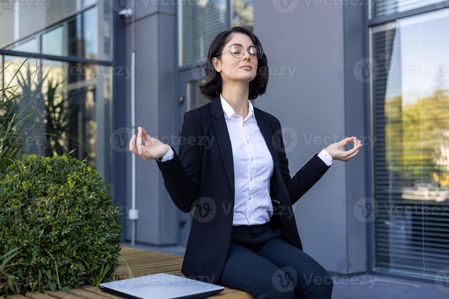 A professional businesswoman in a suit meditates peacefully outdoors, creating a tranquil office escape, balancing productivity and well-being. photo