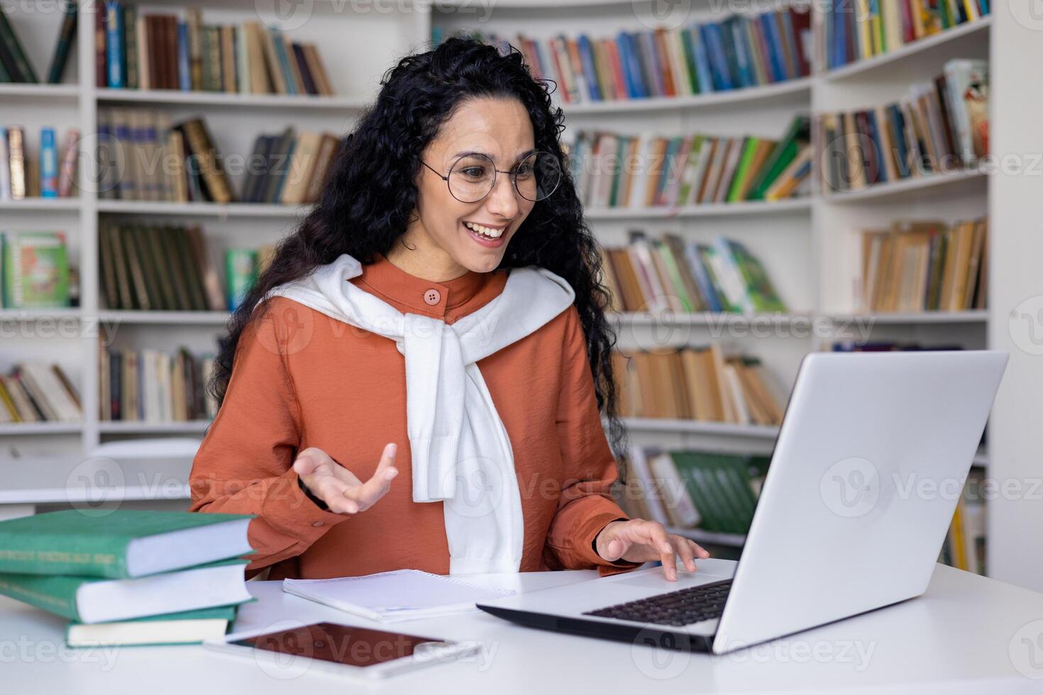 Young Hispanic woman talking on call studying inside university academic library, online learning. photo