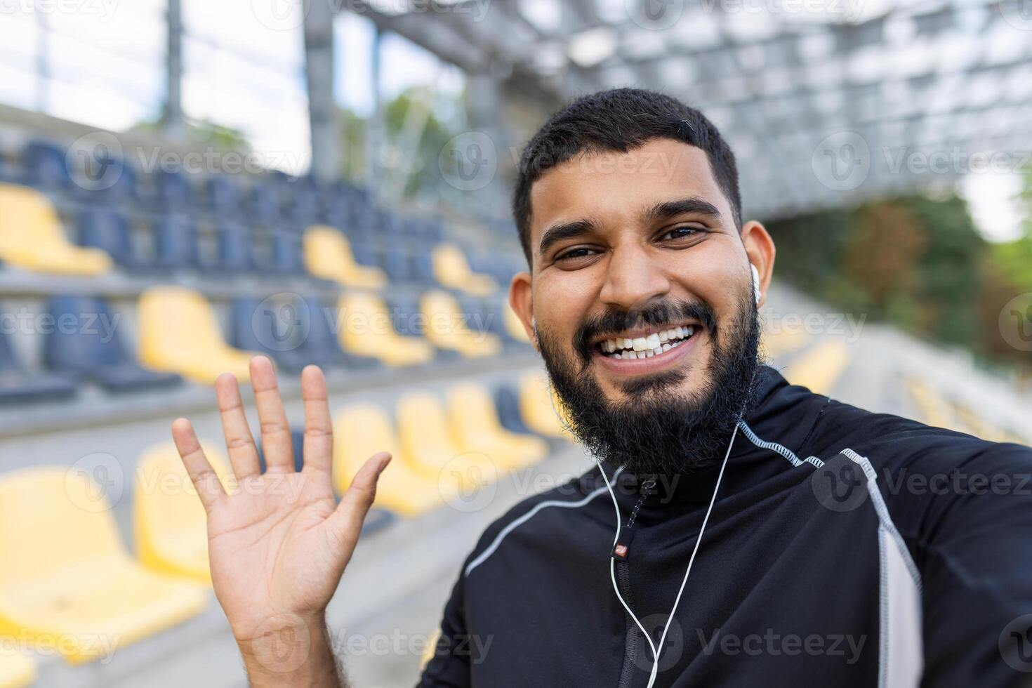Happy man waving while wearing earphones at a stadium photo