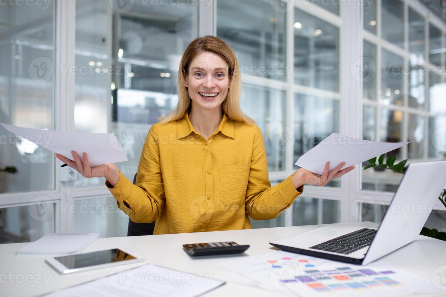 Portrait happy successful woman financier doing paperwork, businesswoman holding papers, documents, contracts and reports in hand, smiling joyfully, satisfied working with laptop, using calculator photo