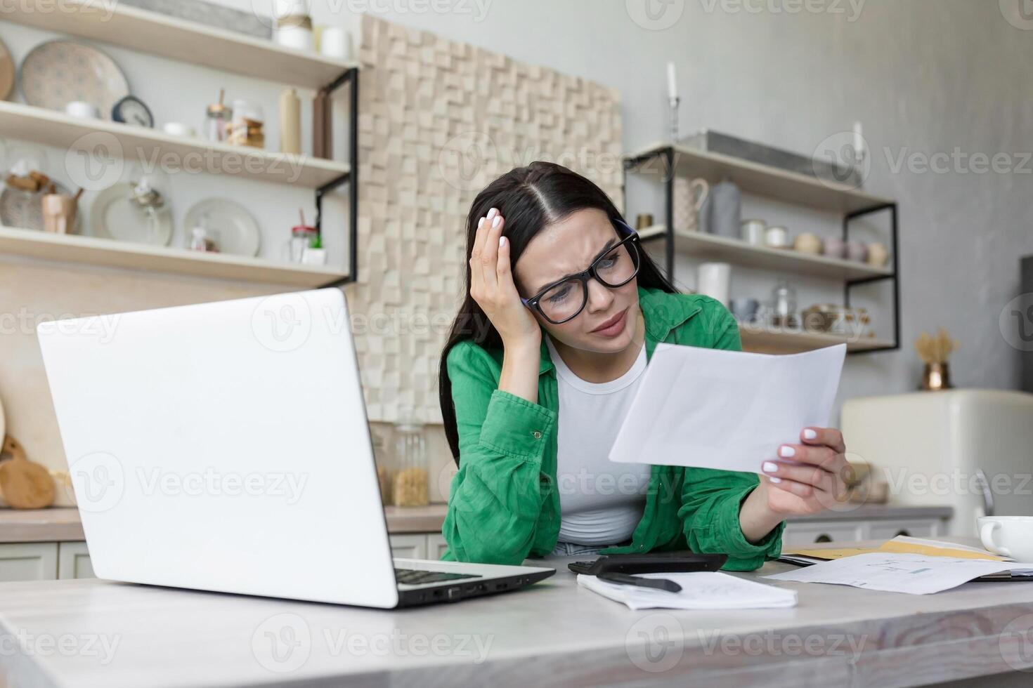 un mujer trabajando a hogar con un ordenador portátil. ella sostiene un carta, un documento en su mano foto