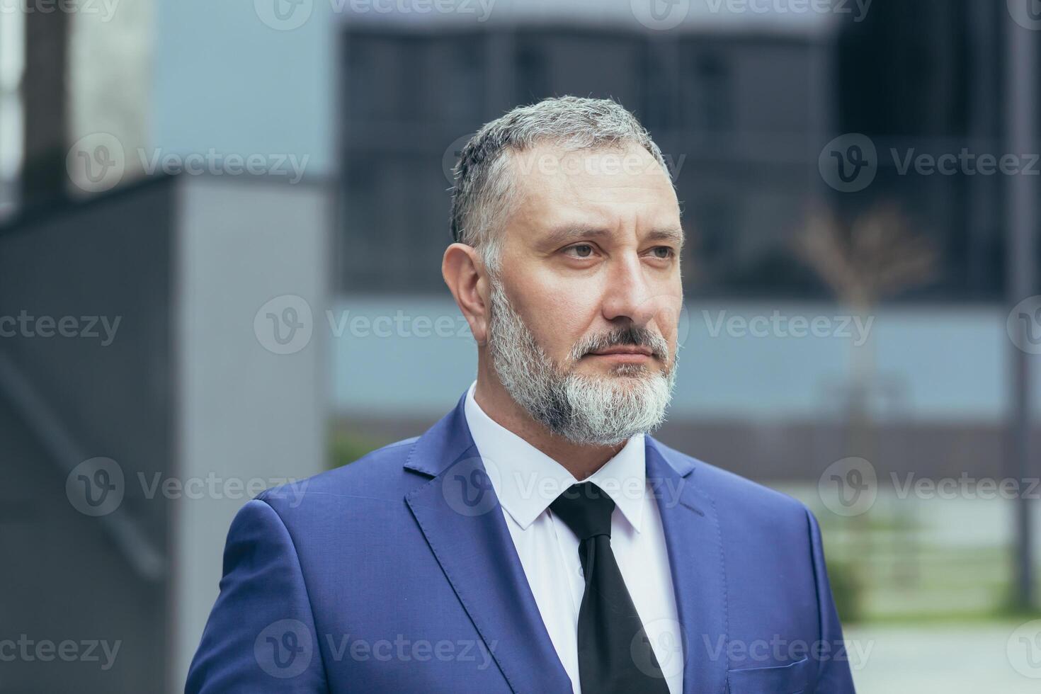 Portrait of senior handsome businessman man with gray hair and brown hair in business suit with tie. Near the office center, looks to the side, serious photo